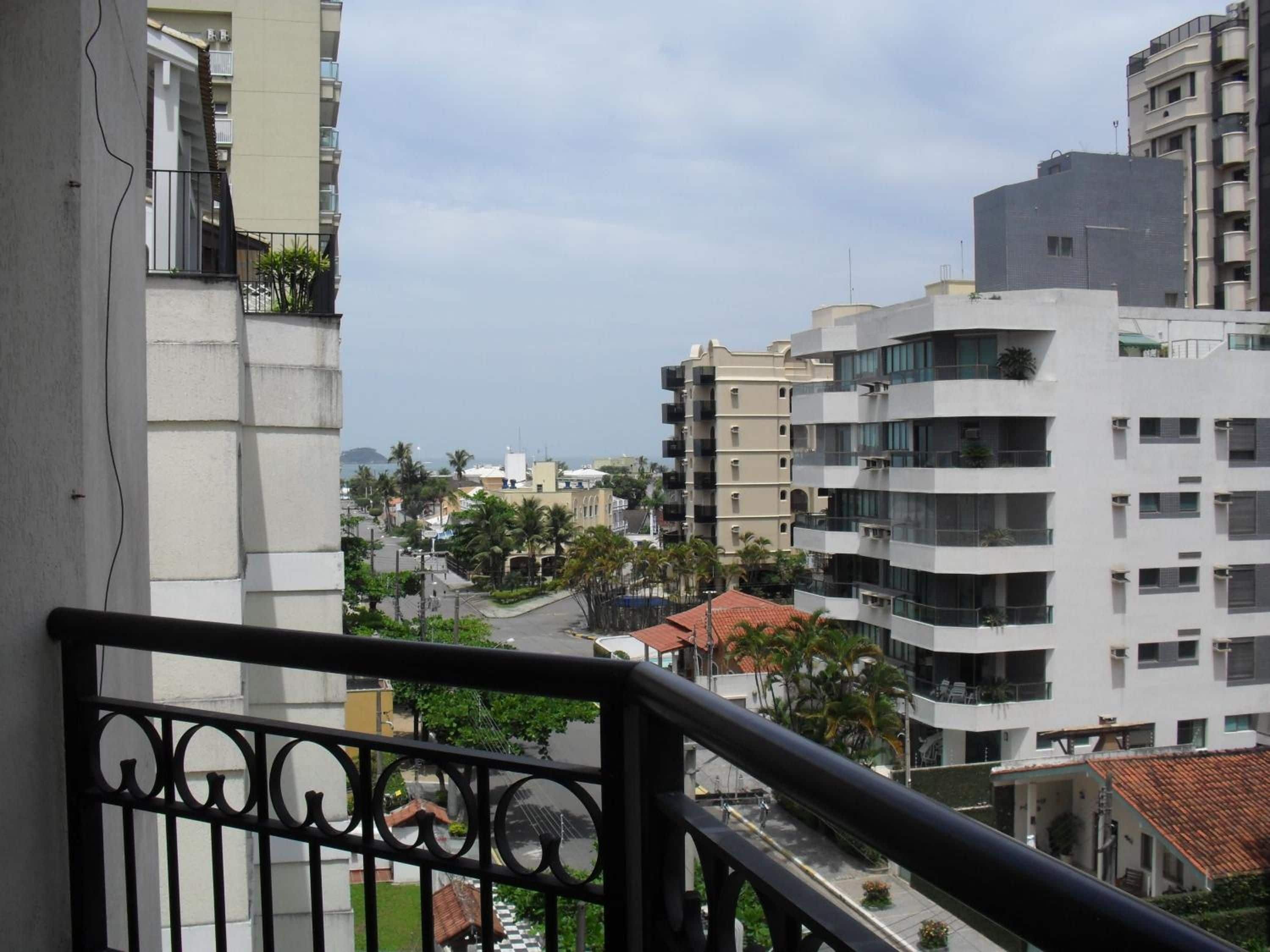 Um edifício de vários andares com varandas, vista para a rua e um corpo d'água ao longe.