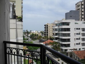 Un edificio de varios pisos con balcones, vista a la calle y una masa de agua distante.