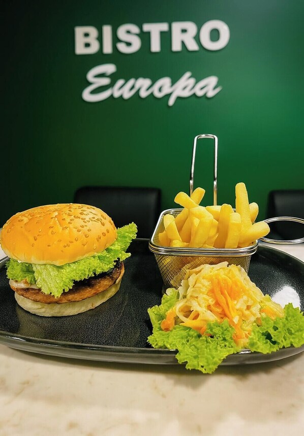 Een schaal met een hamburger, frietjes en geraspte kaas, voor een groene muur met de tekst 
