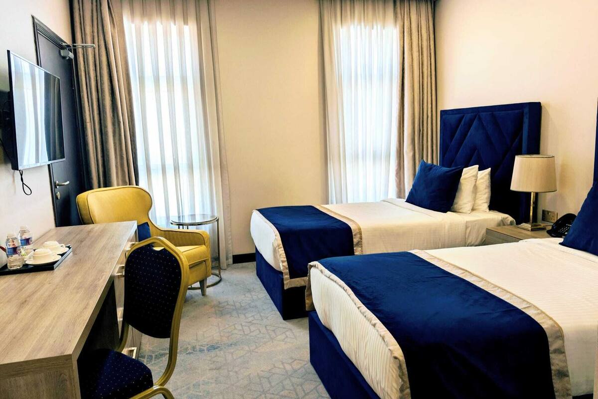 A hotel room with two beds, a desk, a chair, a TV, and a small table.