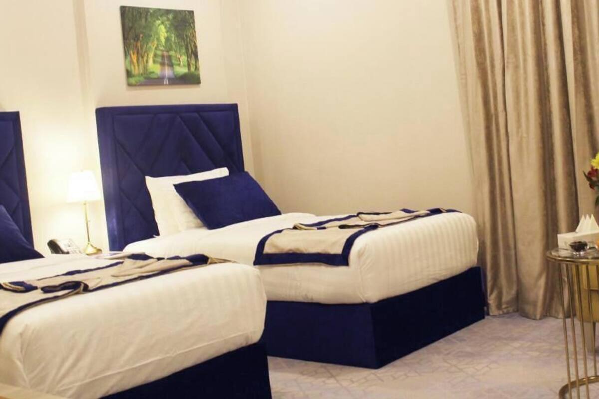 A hotel room with two beds, a small table with a vase, and a yellow chair.