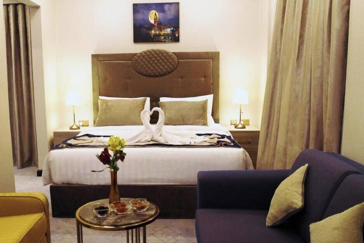 A hotel room with a bed, a sofa, a small table with a vase of flowers, and a painting on the wall.