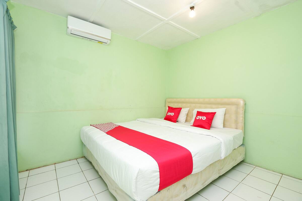 Un dormitorio con cama, colcha roja y blanca, y cabecero color beige.