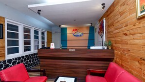 Zona de recepción con un mostrador de madera, asientos rojos, una pared de piedra y un mural colorido.