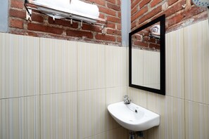 Un baño con un lavabo blanco, un espejo y un perchero de toallas frente a una pared de ladrillo.