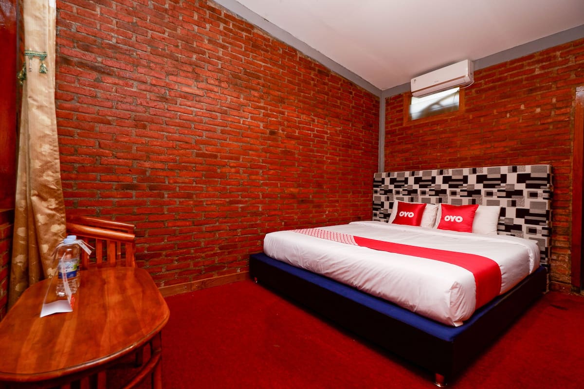 Habitación de hotel con pared de ladrillo, una mesa de madera con una botella y una cama con cabecero estampado.