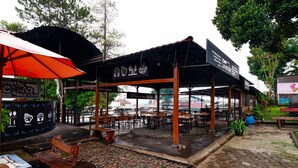 Un café al aire libre con mesas y sillas, una zona de estar cubierta y un letrero que indica opciones de café y comida.
