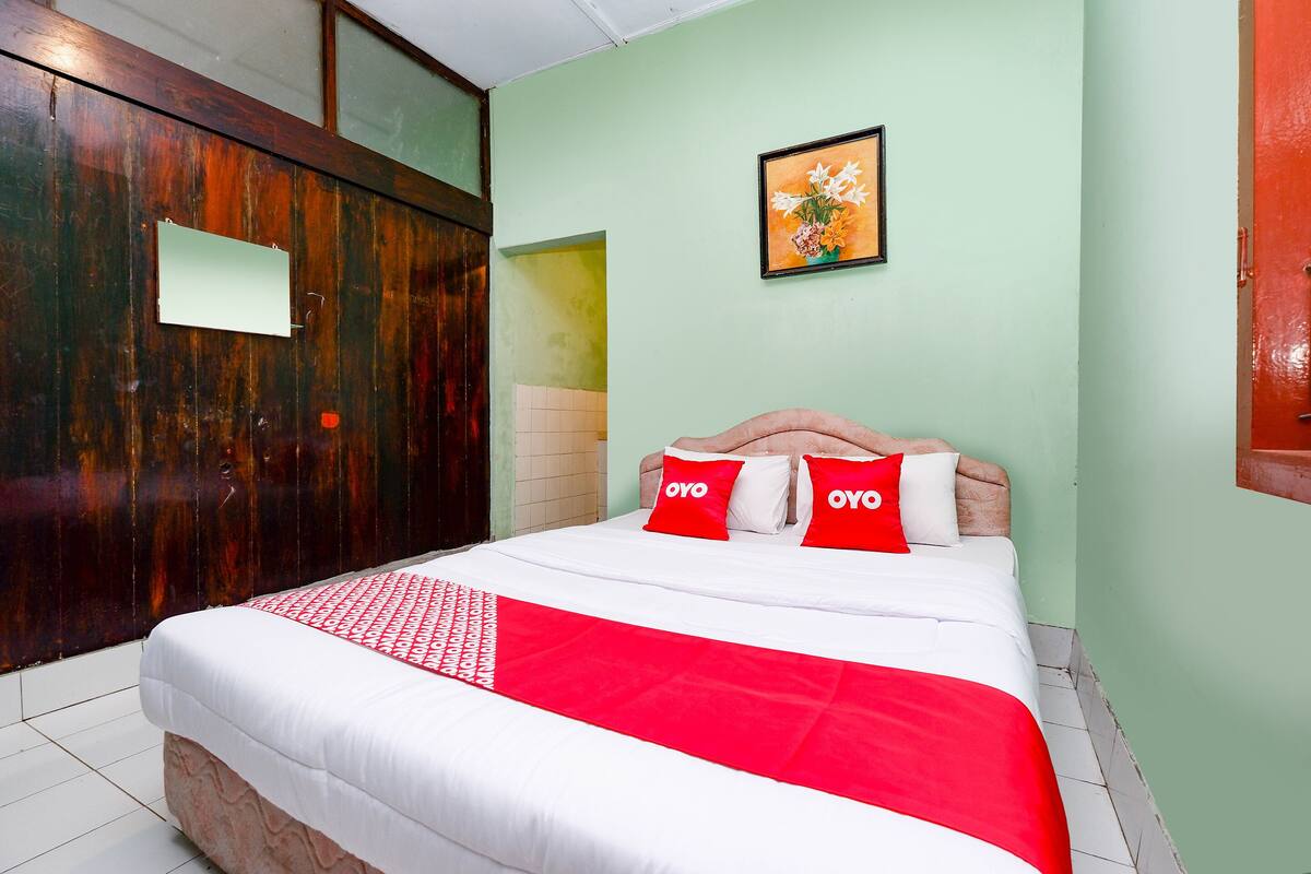 Habitación de hotel con una cama, un armario de madera, una pared verde y un cuadro enmarcado.