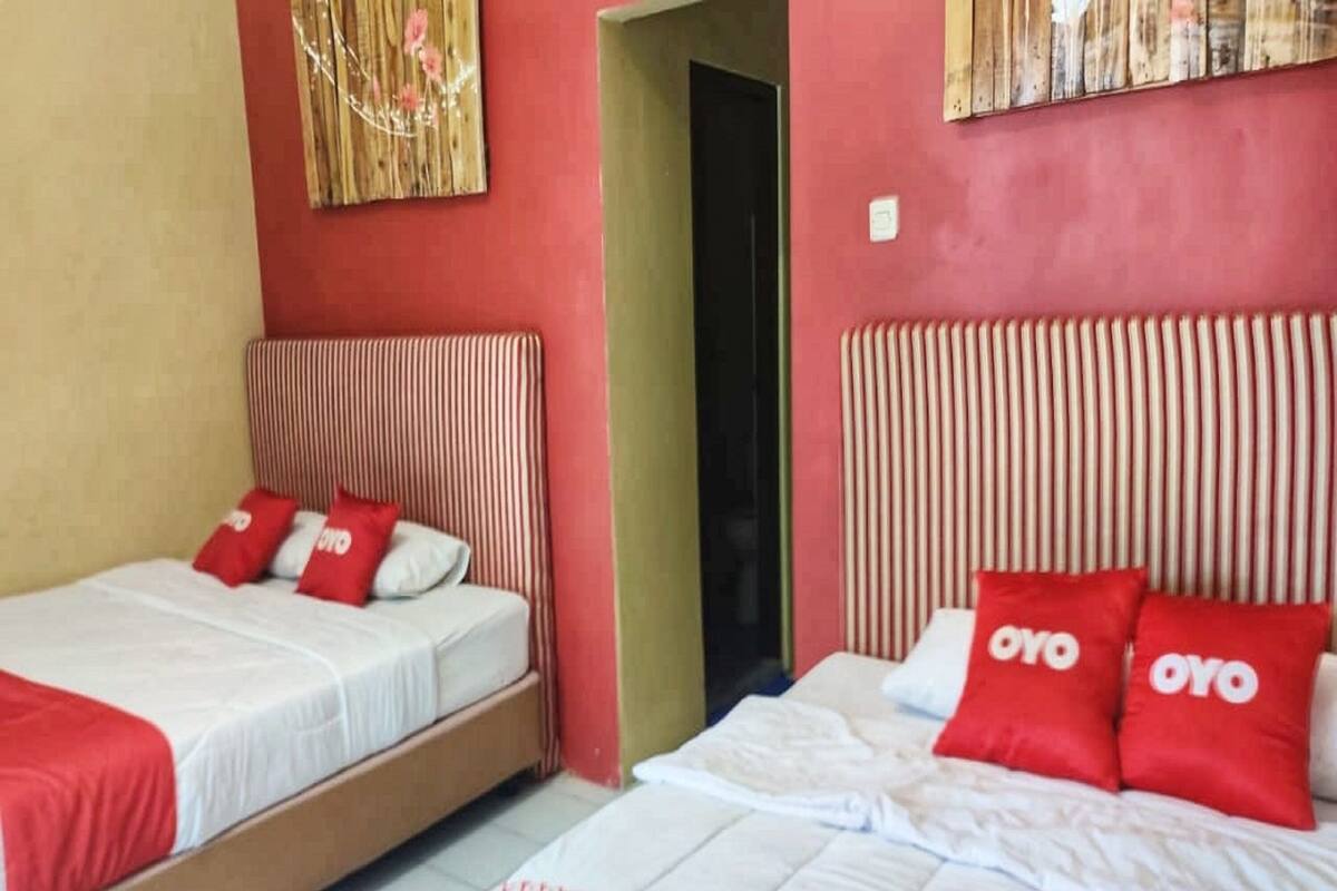 Dos camas individuales con ropa de cama roja y blanca, un tapete estampado y un cabecero de madera.