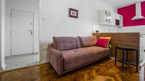 A living room with a brown sofa, a small round table, and a wooden floor. - Crown Apartment (Zagreb)