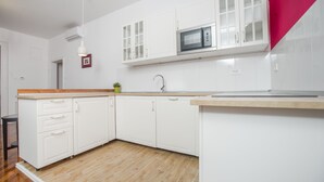 A modern kitchen with white cabinets, a wooden countertop, and a built-in microwave. - Crown Apartment (Zagreb)