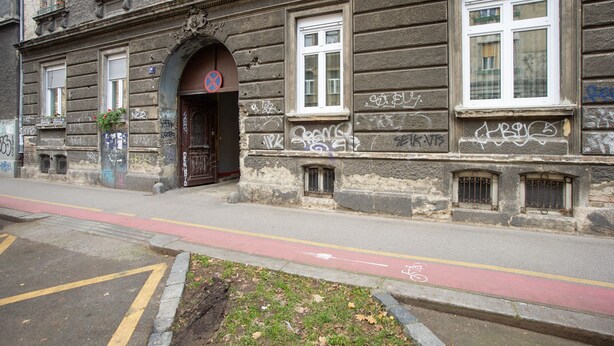 A historic building with a large arched entrance, multiple windows, and graffiti on the facade. - Crown Apartment (Zagreb)
