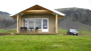 Une cabane en bois avec une véranda, deux chaises et une voiture garée devant.