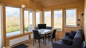 Un intérieur en bois comprenant une table et des chaises, un canapé et de grandes fenêtres donnant sur un champ verdoyant.