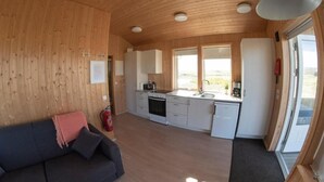 Une cuisine de taille réduite avec des meubles blancs, une cuisinière et un évier. On y trouve un canapé avec une couverture et des coussins, ainsi qu’un extincteur accroché au mur.