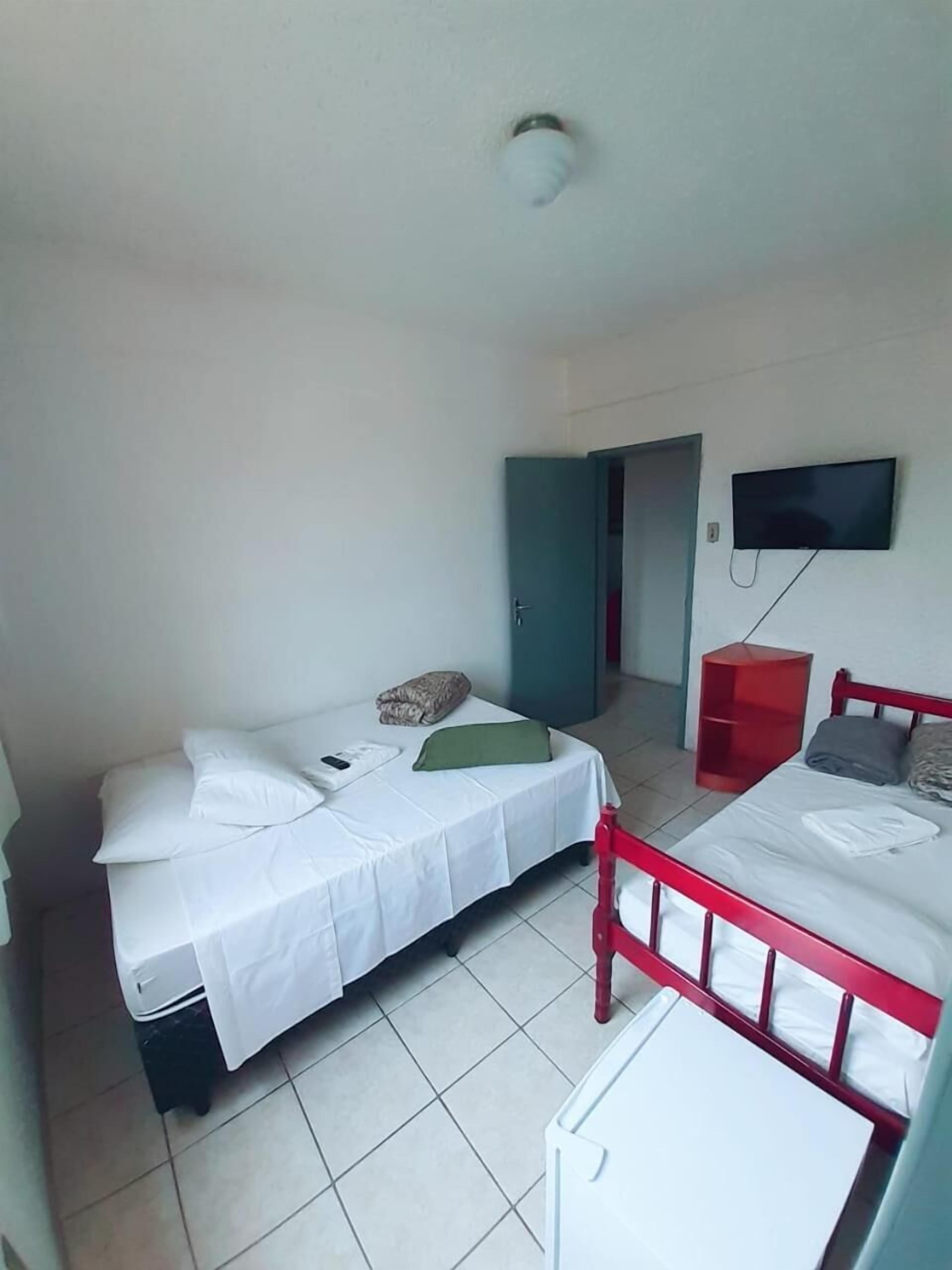 A small, clean room with two beds, a TV, and a red chair.