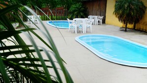 Una piscina con sillas blancas y una pequeña mesa, rodeada por un solárium de hormigón y una valla de madera.
