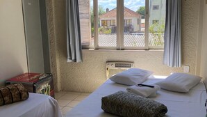 Habitación de hotel con dos camas individuales, una ventana con cortinas, un radiador y una mesita con una caja.