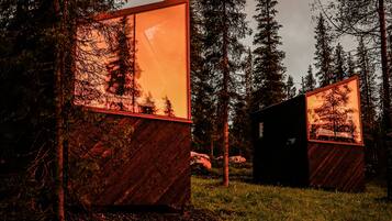 Une cabane dotée de grandes fenêtres qui reflètent un paysage boisé.