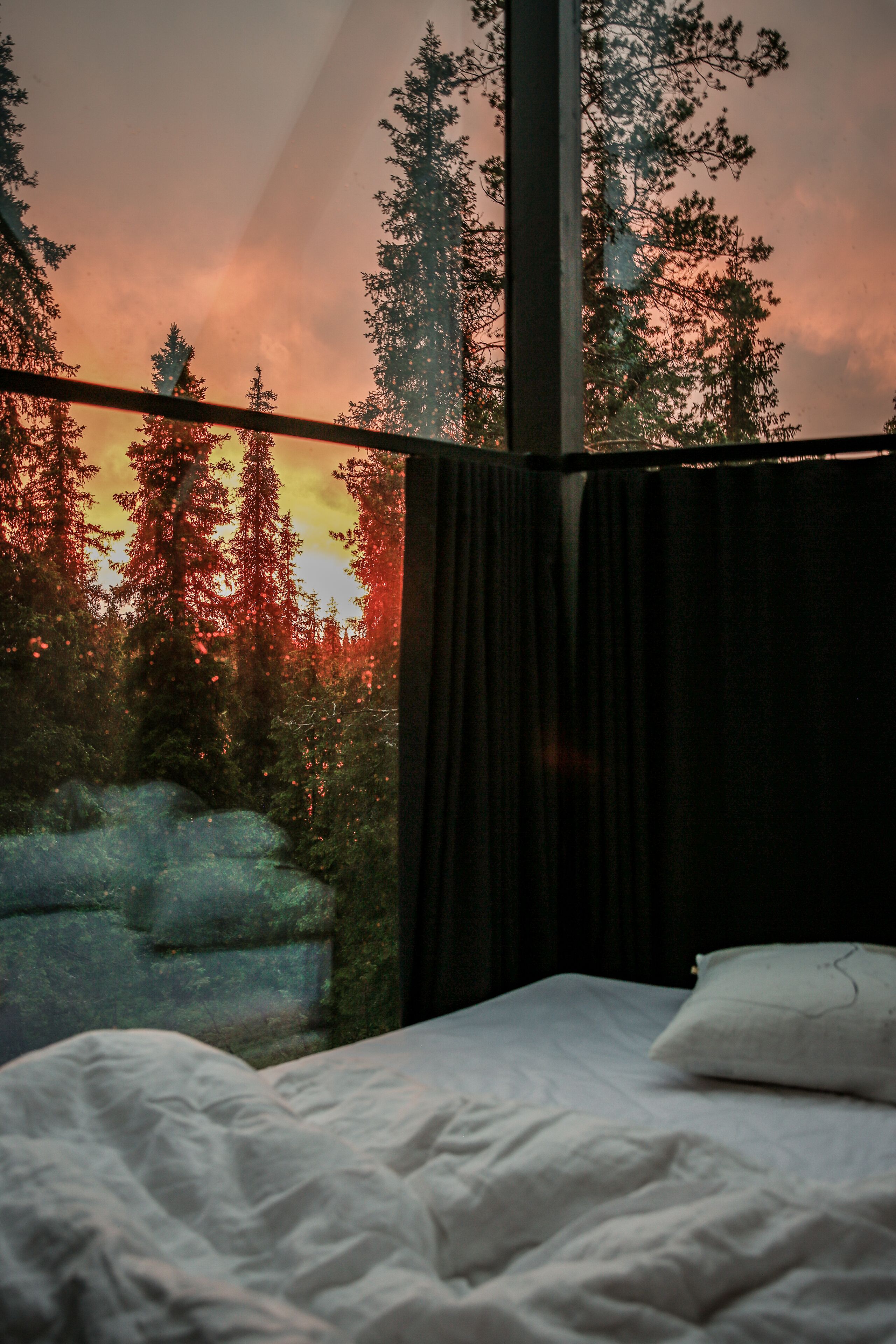 A bedroom with a large window overlooking a forest and a sunset.