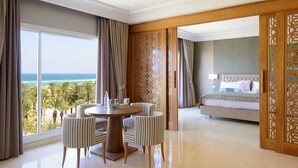 A hotel room with a large window offering a view of the ocean, a round dining table with striped chairs, and a bed with a headboard. - Occidental Sousse Marhaba (Sousse)