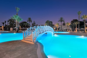 A swimming pool with a white bridge, palm trees, and a building in the background. - Occidental Sousse Marhaba (Sousse)