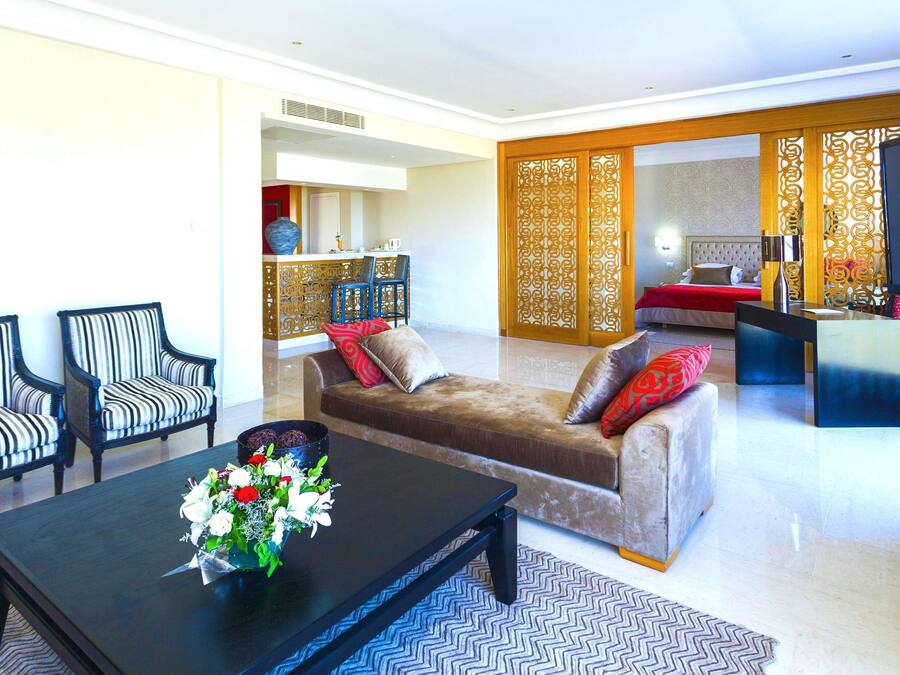 A modern living room with a sofa, two striped armchairs, a coffee table with a vase of flowers, and a television.
