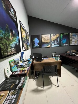 Una habitación con escritorio, computadora, silla y carteles en la pared.