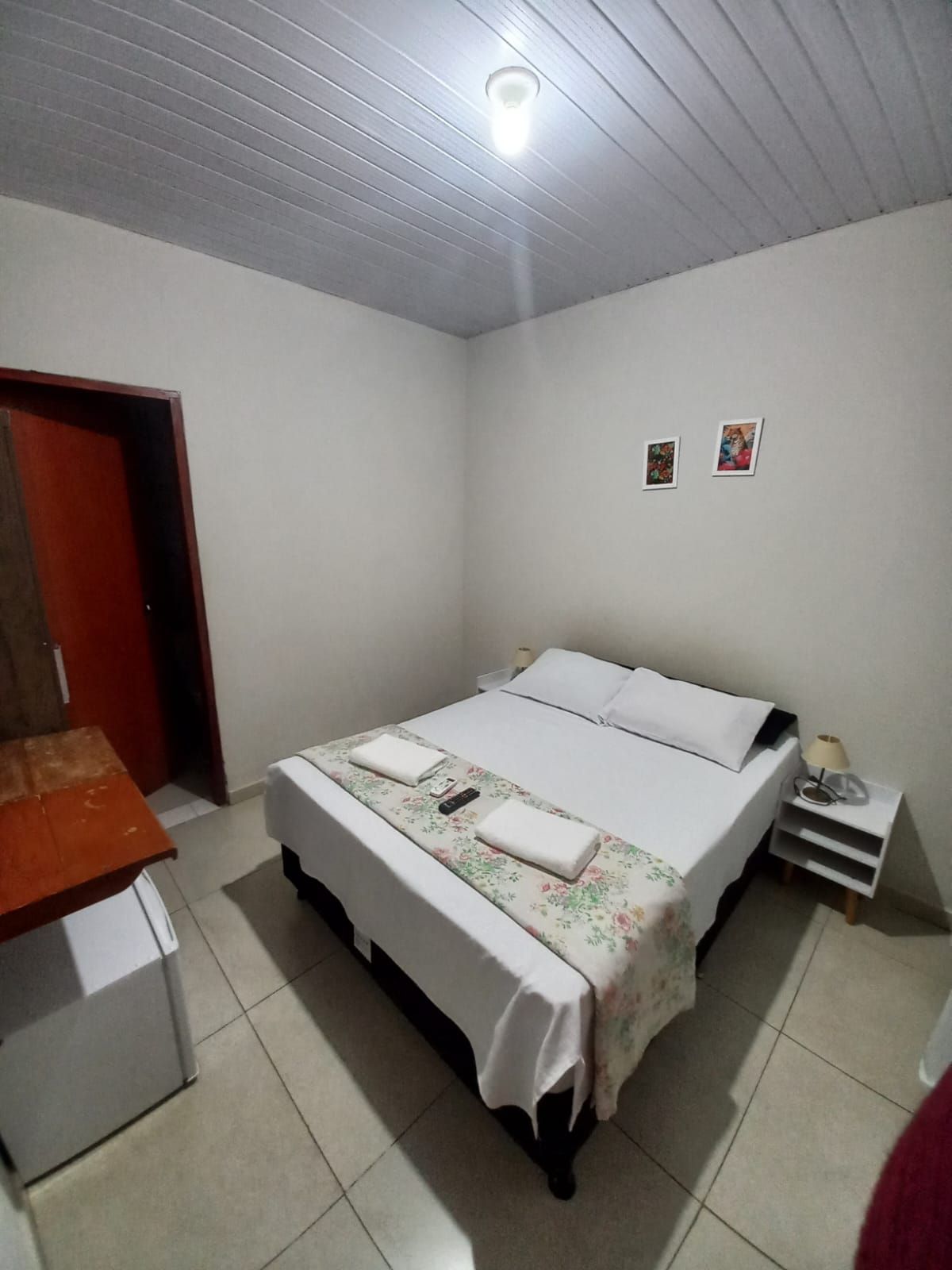 A single-bed room with a wooden nightstand, a small table, and a door leading to another room.