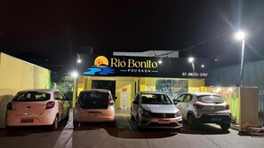 A hotel entrance with a sign reading 'Rio Bonito Pousada' and a contact number. There are three cars parked in front. - Pousada Rio Bonito (Bonito)