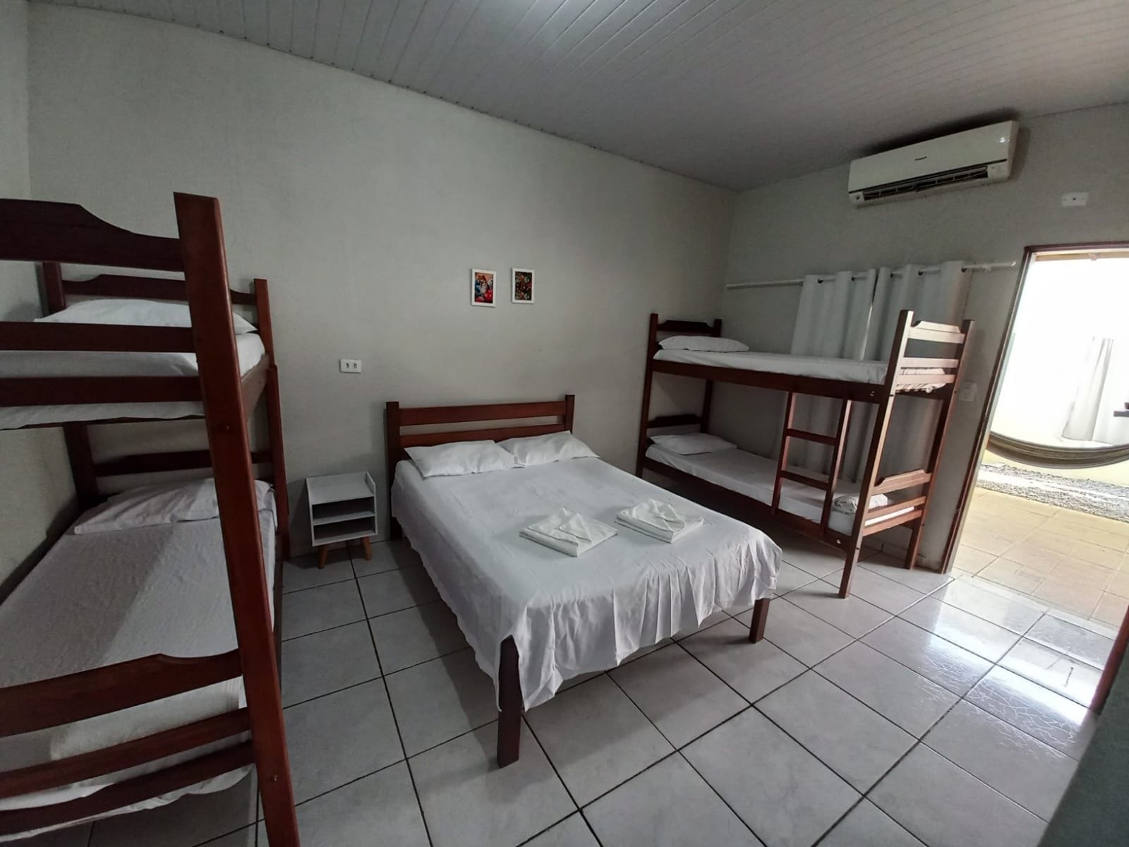 Une chambre avec des lits superposés, un lit simple, une petite table de chevet et un appareil de climatisation.