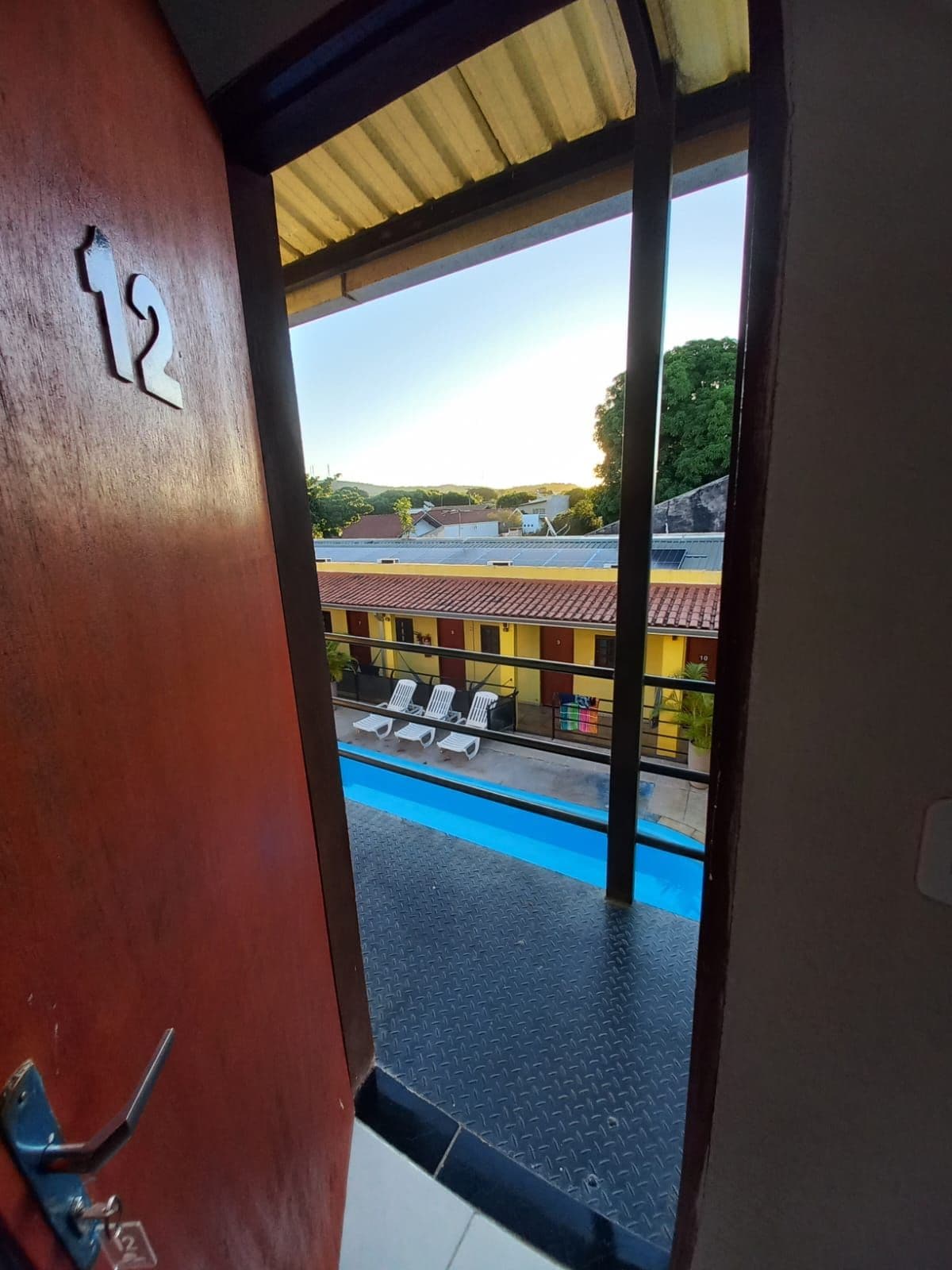 A hotel room with a view of a swimming pool and a building with red roofs.