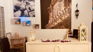 Een kamer met een houten dressoir, een stoel, een klein tafeltje met een mand, en een muur met ingelijste foto's en een groot muurschildering.