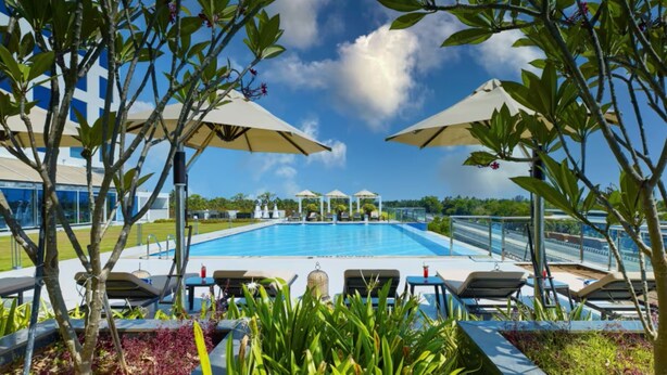 Una piscina con lettini e ombrelloni, circondata da vegetazione e un cielo sereno.
