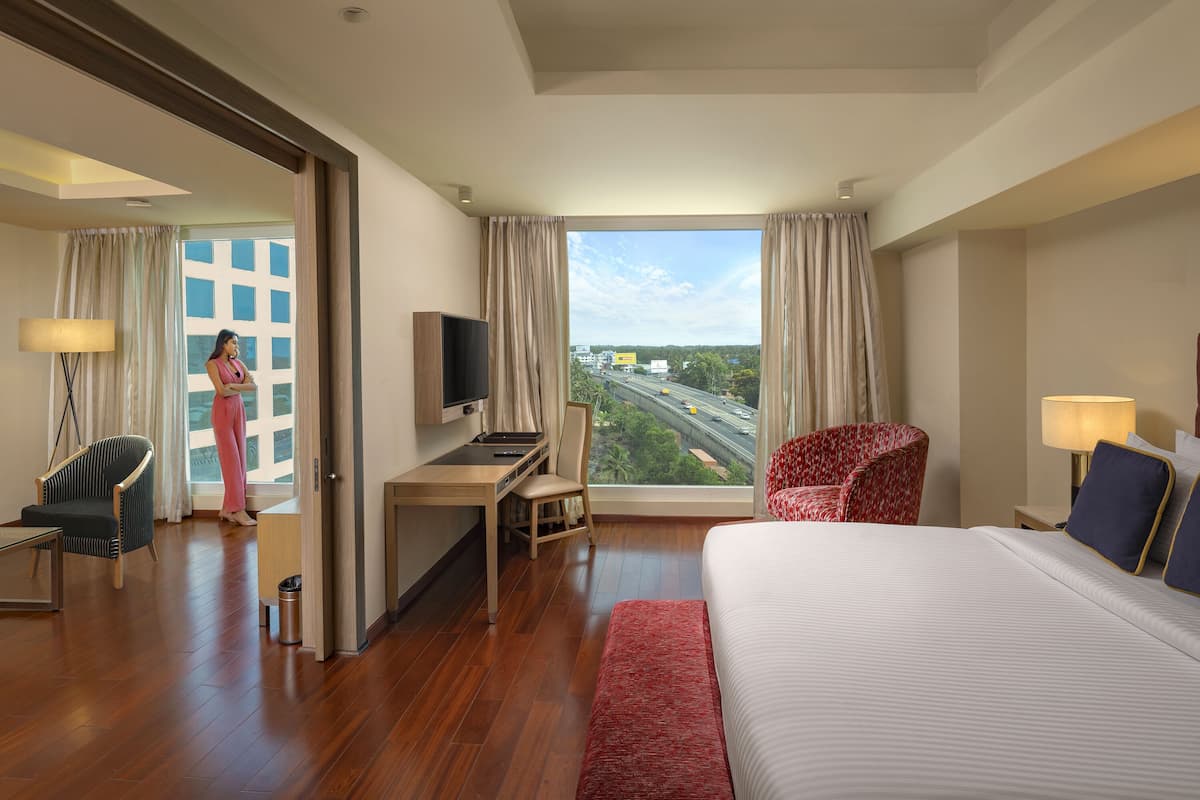 A hotel room with a large bed, a desk with a TV, a chair, and a view of a highway.