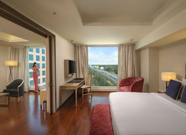 Una habitación de hotel con una cama grande, un escritorio con televisión, una silla y vistas a una autopista.