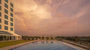 A modern hotel with a large outdoor swimming pool, a well-maintained lawn, and a view of a road with vehicles.