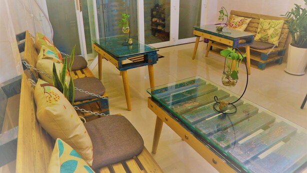 Una sala de estar moderna con una mesa de centro de vidrio, sofá de madera y una pequeña mesa con una planta.