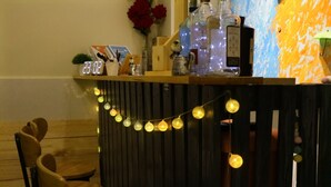 Un banco de madera y una mesa con un reloj, luces decorativas y varios objetos en una estantería.