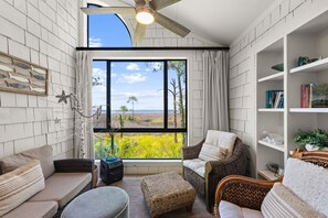 A room with a large window, wicker furniture, a ceiling fan, and a bookshelf. - Bay View ~ Sunroom ~ Golf Cart (Miramar Beach)