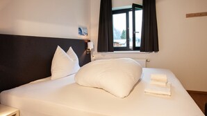 A neatly made bed with white linens and pillows, a bedside lamp, and a window with curtains.