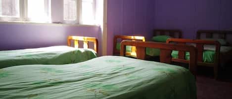 Una habitación con dos camas de madera, ropa de cama verde, un ventanal con marcos blancos y paredes moradas.