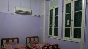 Una habitación con dos camas de madera, una ventana con persianas verdes y un equipo de aire acondicionado en la pared.