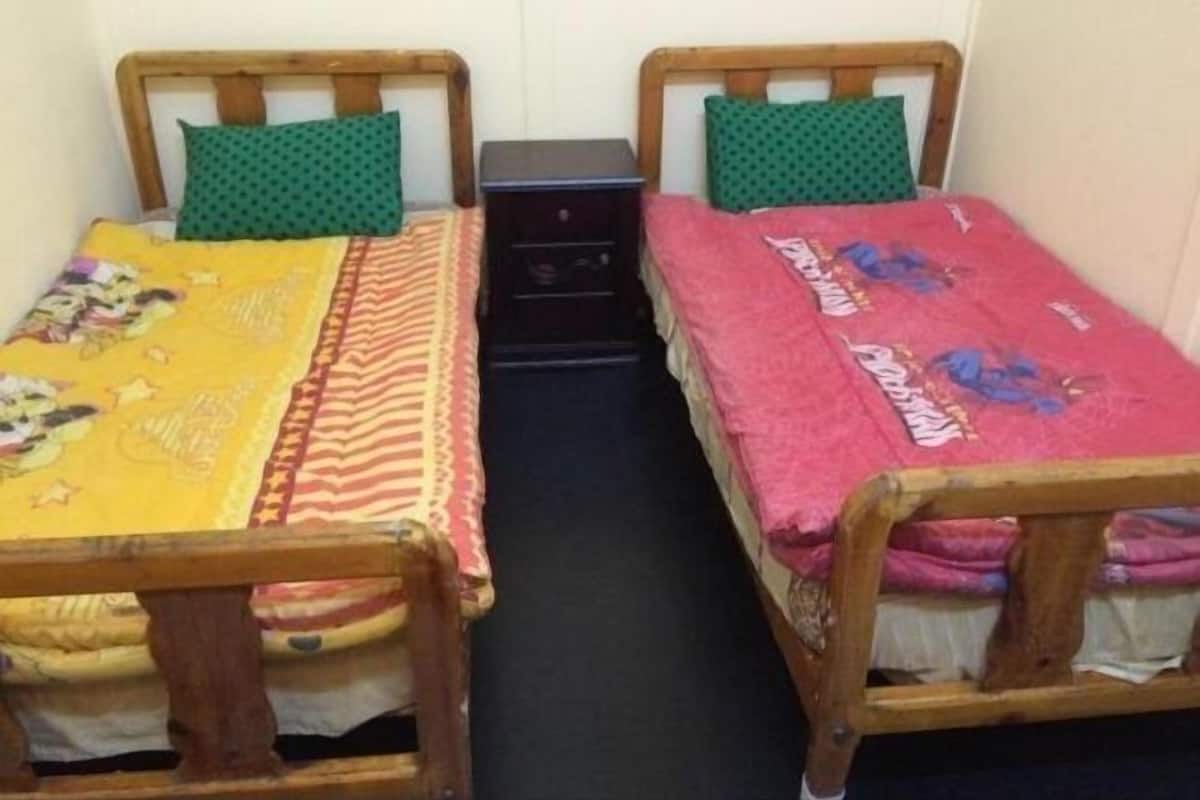 Deux lits simples avec des cadres en bois et des oreillers verts, une petite table de chevet noire et un mur sobre.