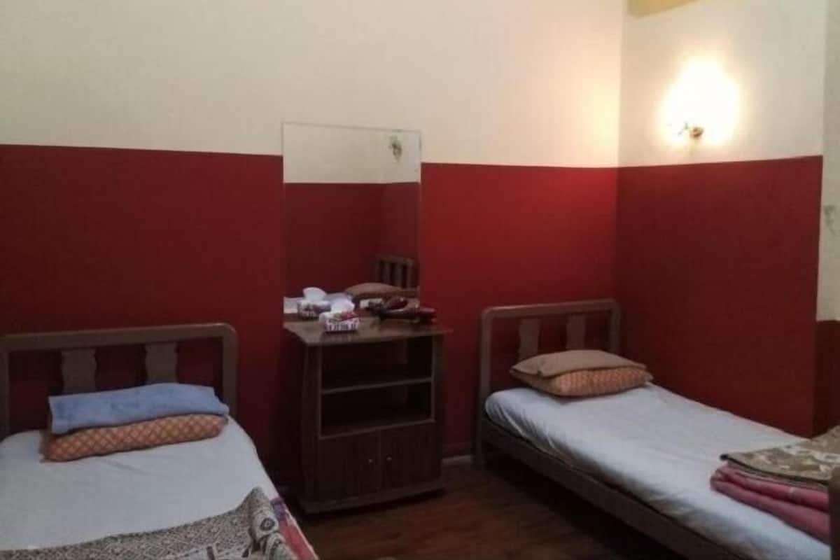 Un petit logement composé d’une seule pièce, comprenant deux lits, une armoire en bois et un climatiseur fixé au mur.