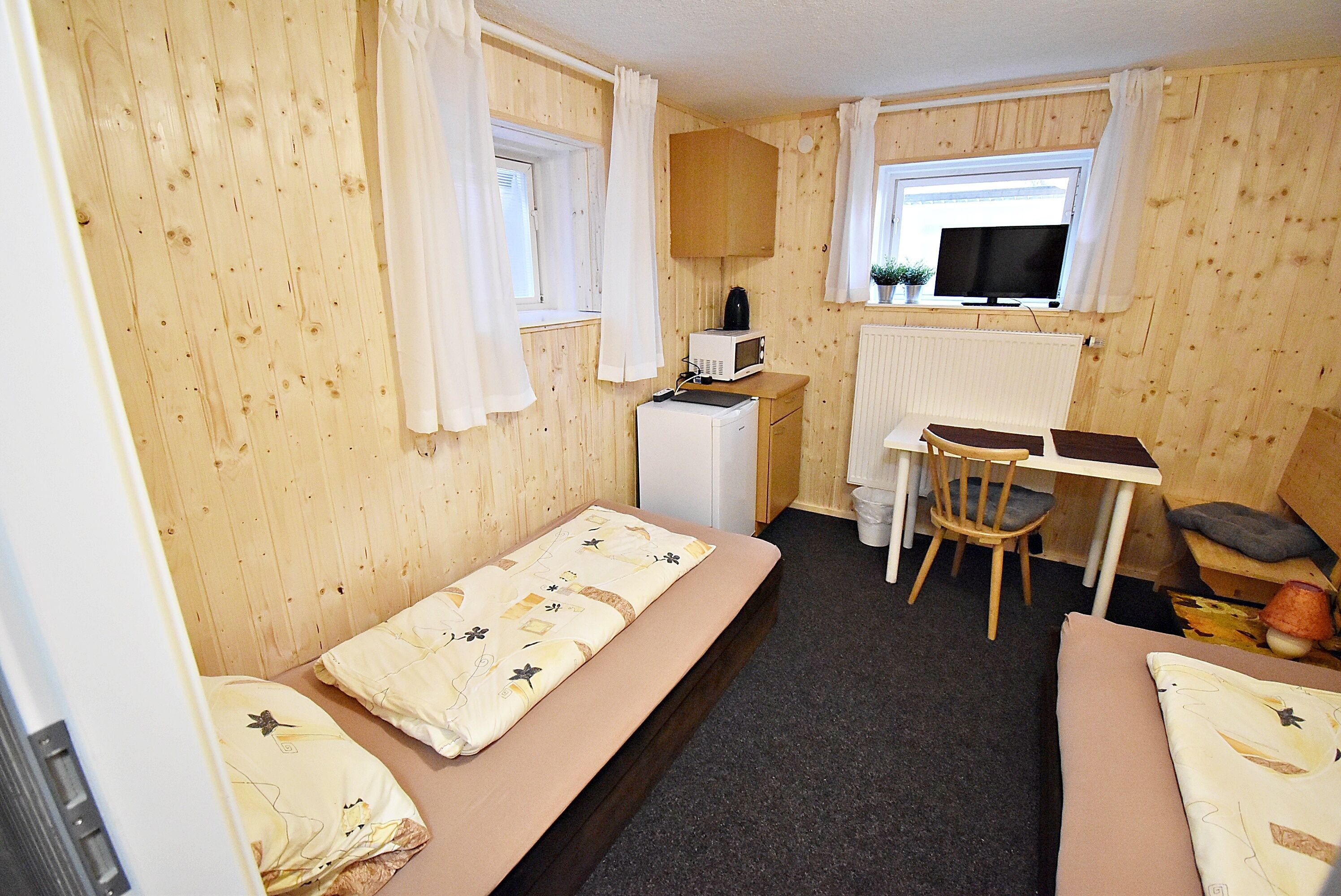 A compact room with a bed, a small desk, a chair, and a television.