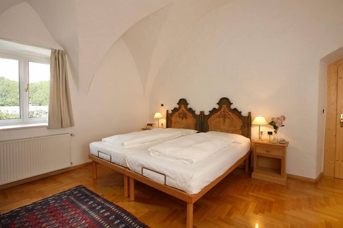 Una camera da letto con un letto in legno, due comodini con lampade, una finestra con tende e un termosifone.