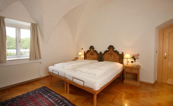 Ein Schlafzimmer mit einem hölzernen Bett, zwei Nachttischen mit Lampen, einem Fenster mit Vorhängen und einer Heizung.