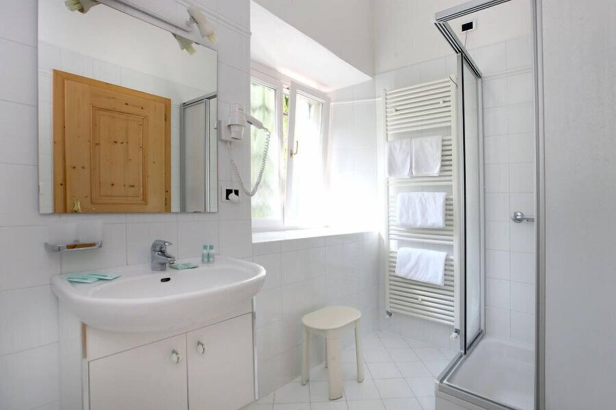 Un bagno moderno con un lavandino bianco, un mobiletto in legno, uno specchio, una finestra e un box doccia in vetro.