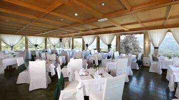 Une salle de banquet avec de nombreuses tables rondes, des nappes blanches et des chaises recouvertes de housses blanches.